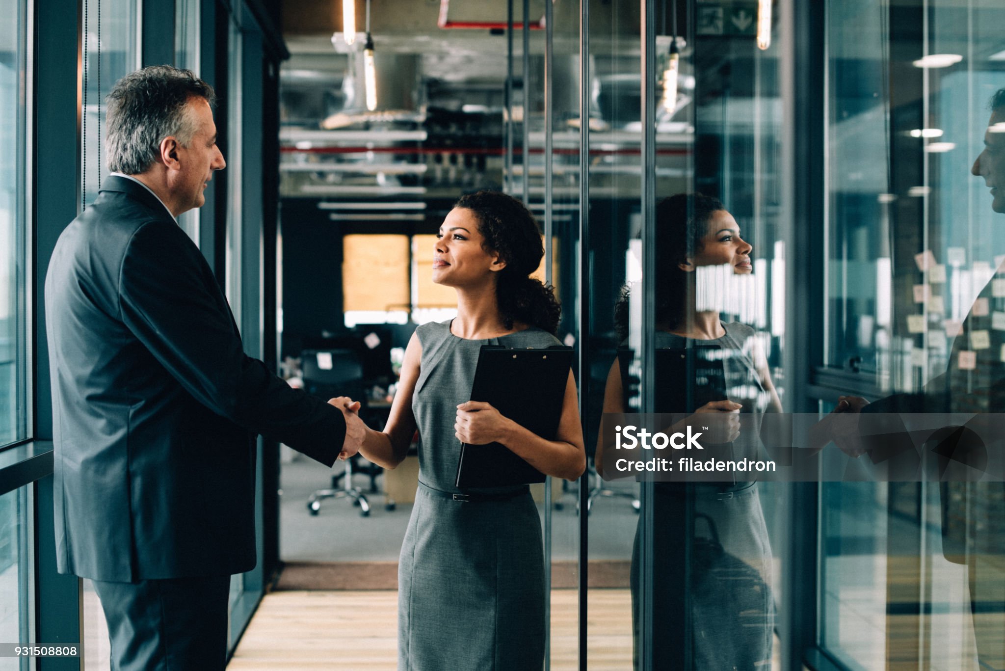Business professionals shaking hands in modern glass office hallway
