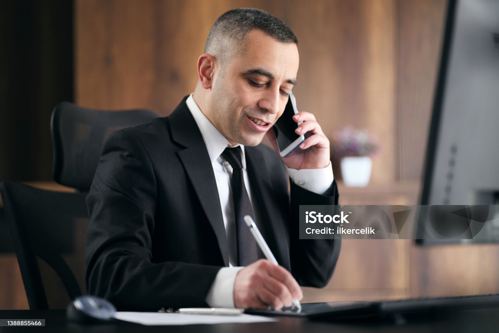 Professional businessman in suit talking on phone while taking notes