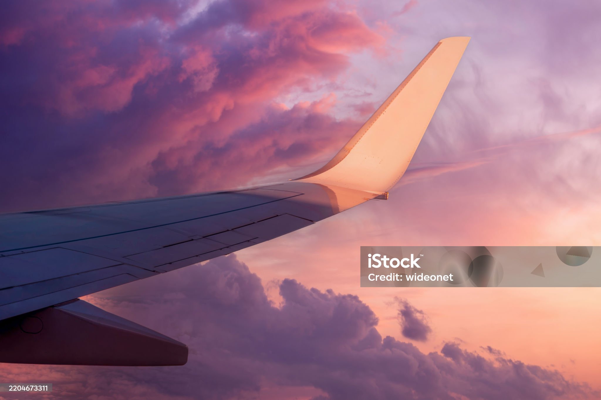 Airplane wing view at sunset with pink and purple clouds