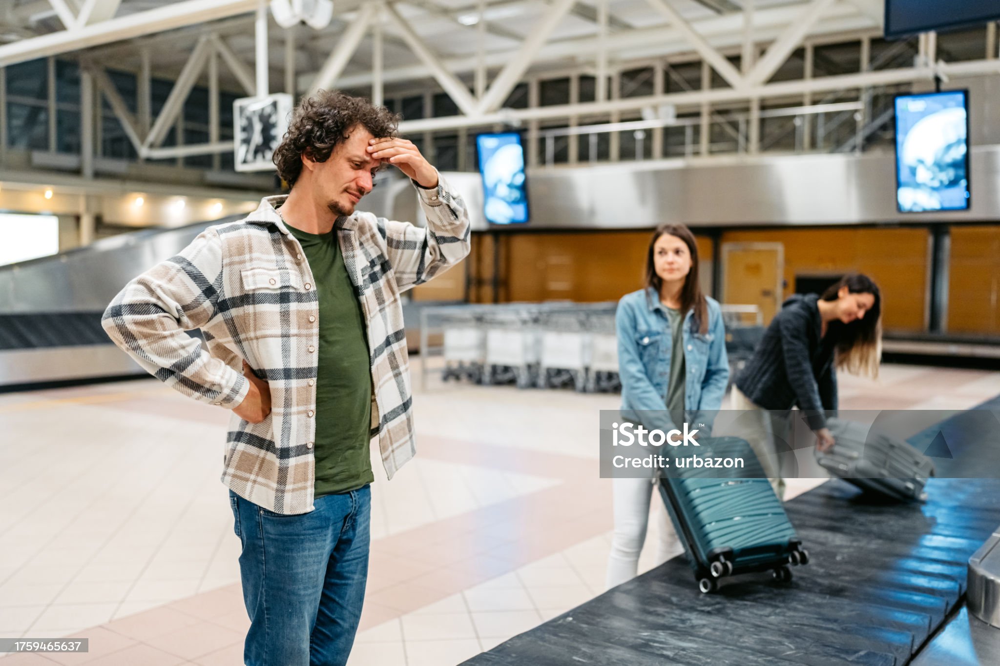 Frustrated man waiting for luggage at airport baggage claim carousel
