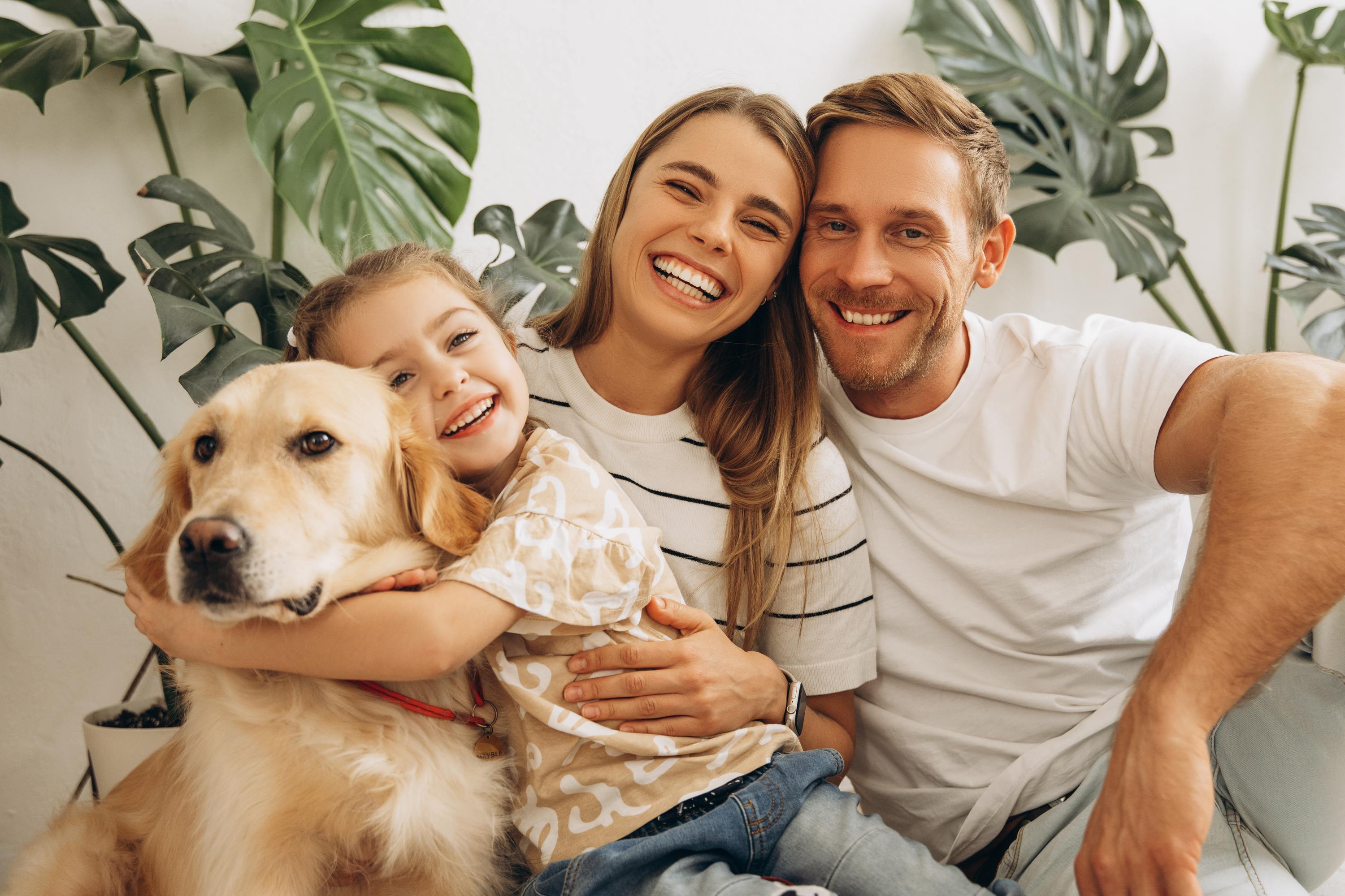 Happy family with golden retriever dog and tropical plants in background