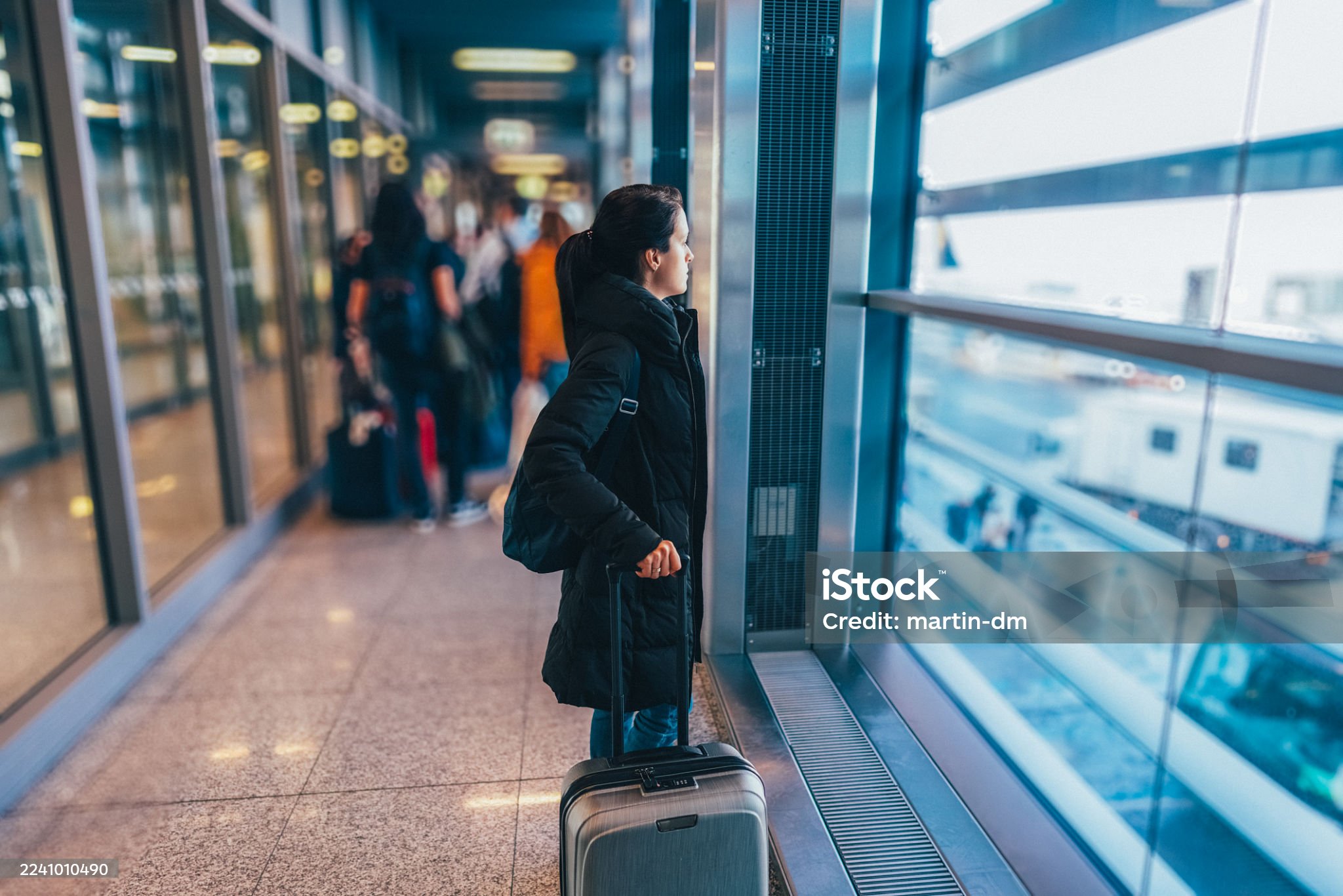 Woman in black coat waiting at airport gate with luggage