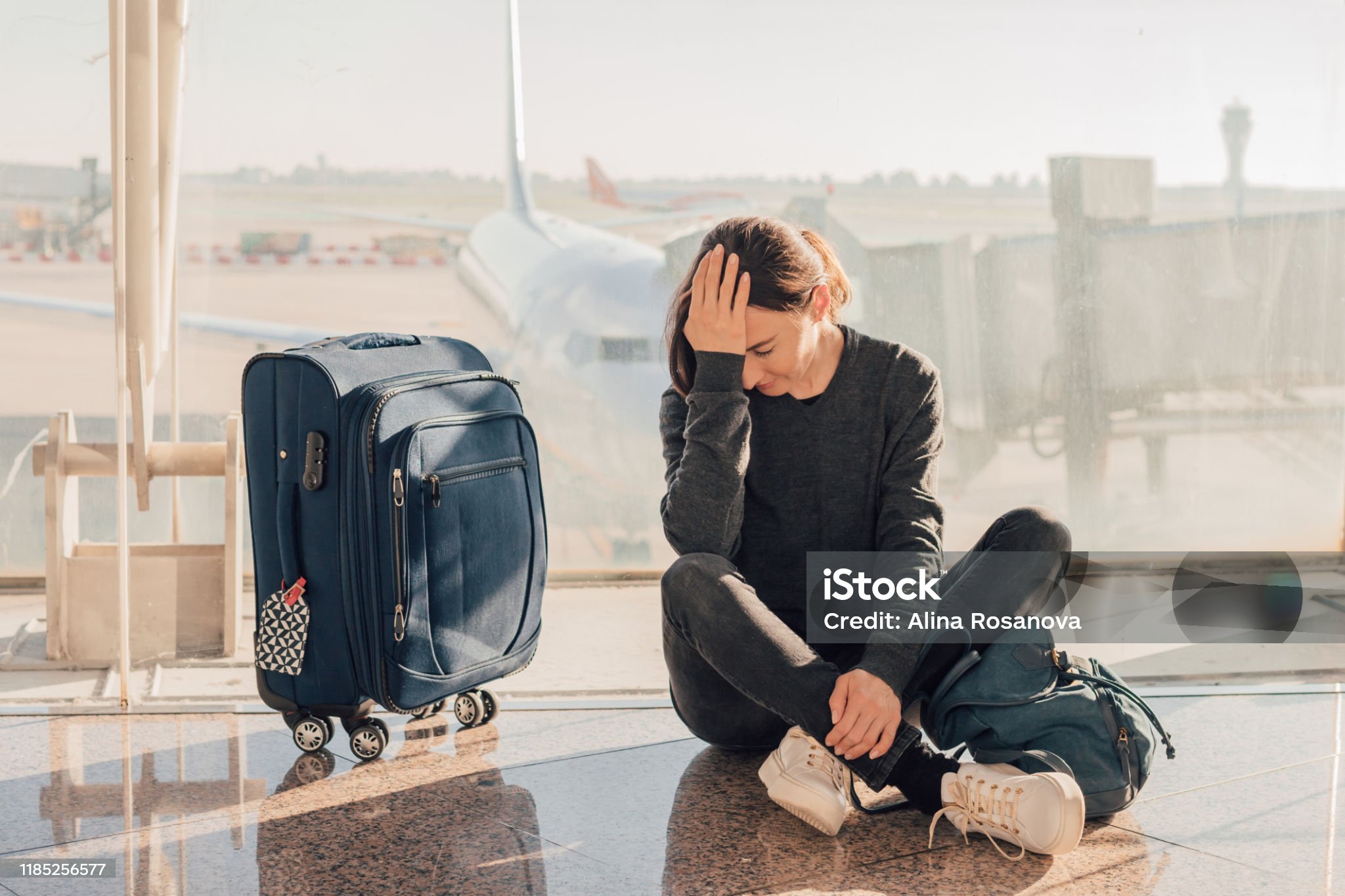 Woman sitting stressed at airport with luggage waiting for delayed flight